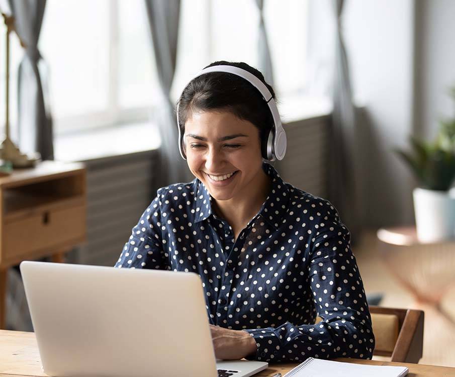 Smilende dame med hodetelefoner sitter foran datamaskinen